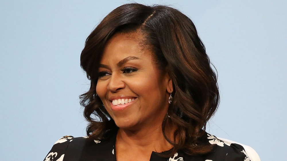 Michelle Obama in un abito nero floreale stampato, sorridente mentre si guarda di lato