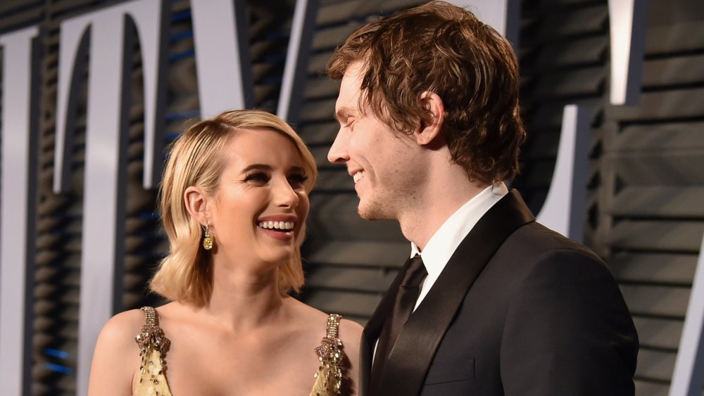 Emma Roberts in abito d'oro e Evan Peters in abito nero, sorridendo l'un l'altro sul tappeto rosso