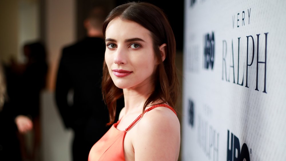 Emma Roberts in un abito rosso con i capelli bruni, in posa dal lato a un passo-e-ripetere