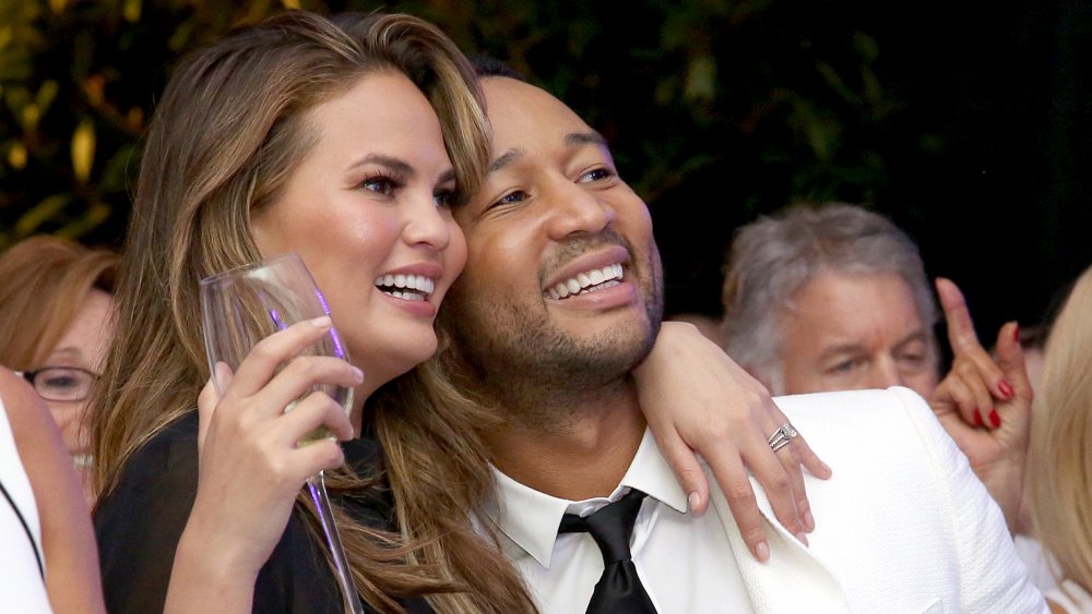 Chrissy Teigen tiene in mano un bicchiere di champagne, abbracciando John Legend