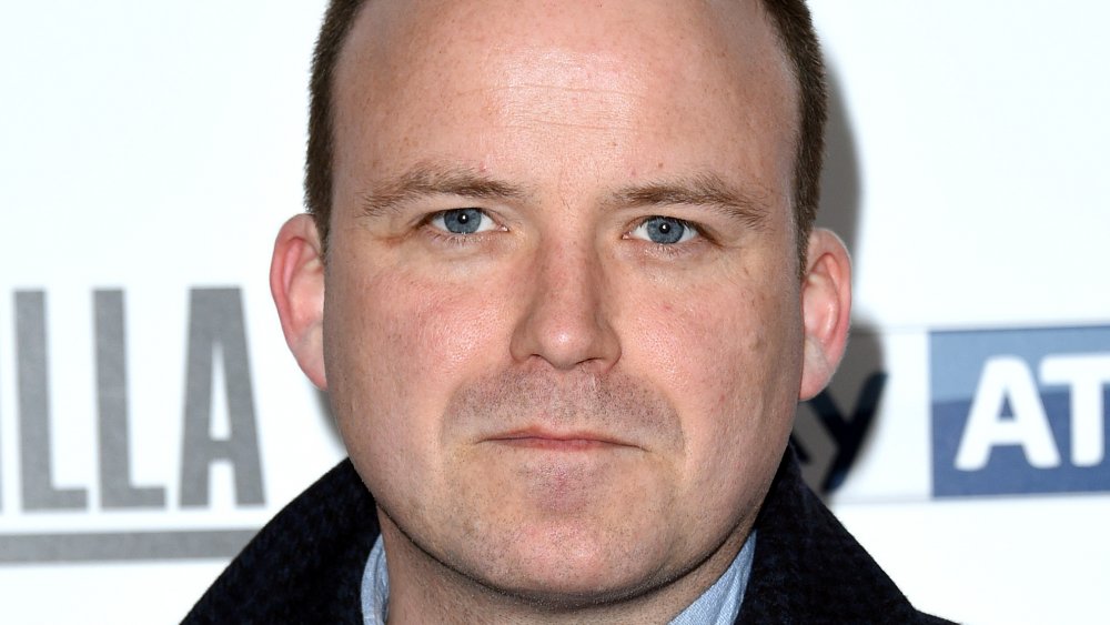 Rory Kinnear in un cappotto a scacchi in bianco e nero, in posa con un'espressione neutra