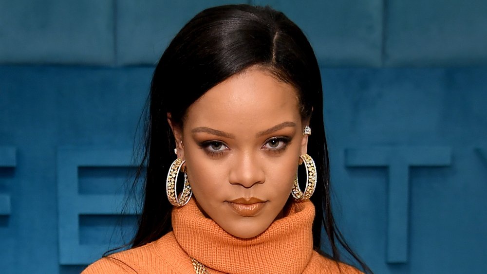 Rihanna in un abito a collo di tartaruga arancione, in posa con un'espressione seria