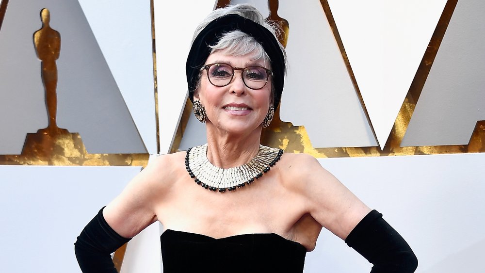 Rita Moreno in abito nero, sorridente e in posa con entrambe le mani sui fianchi agli Oscar