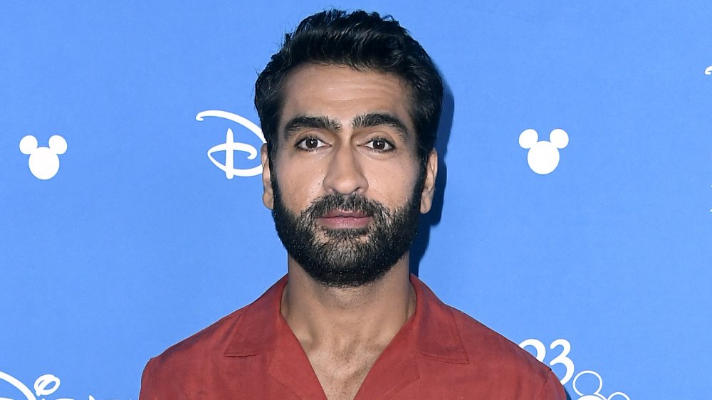 Kumail Nanjiani in un button-up rosso, in posa a un evento Disney con un'espressione neutra