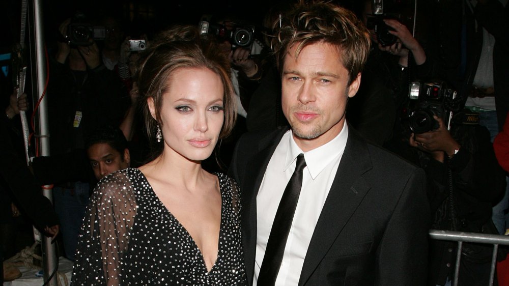 Angelina Jolie e Brad Pitt, in posa insieme a espressioni serie, circondati da fotografi