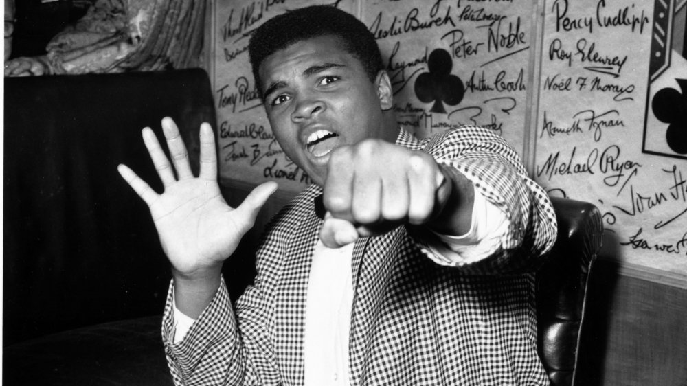 Foto in bianco e nero di Muhammad Ali in abiti da strada, che colpisce una posa giocosa di boxe