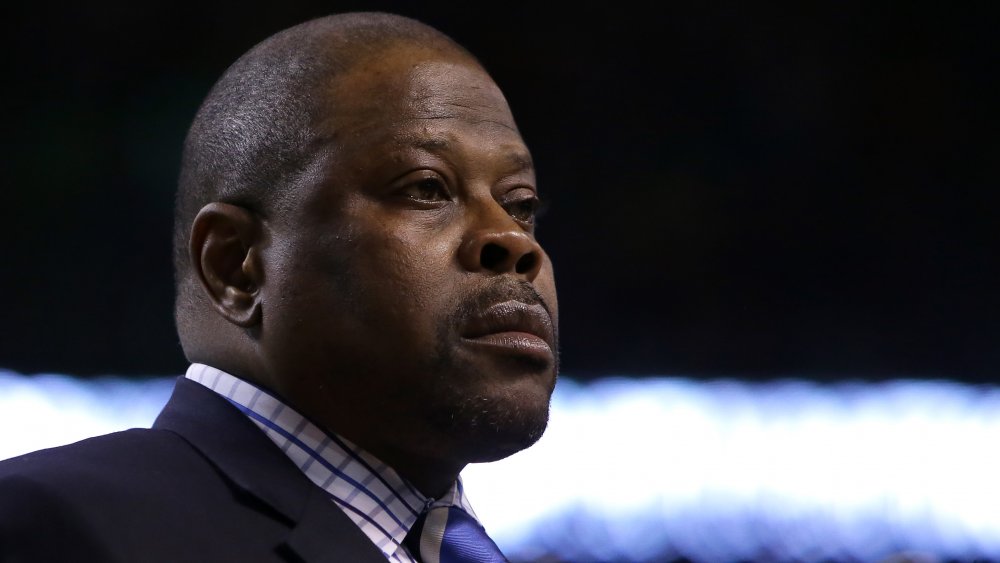 Patrick Ewing in un blazer blu e camicia a scacchi, guardando fuori di lato con un'espressione seria