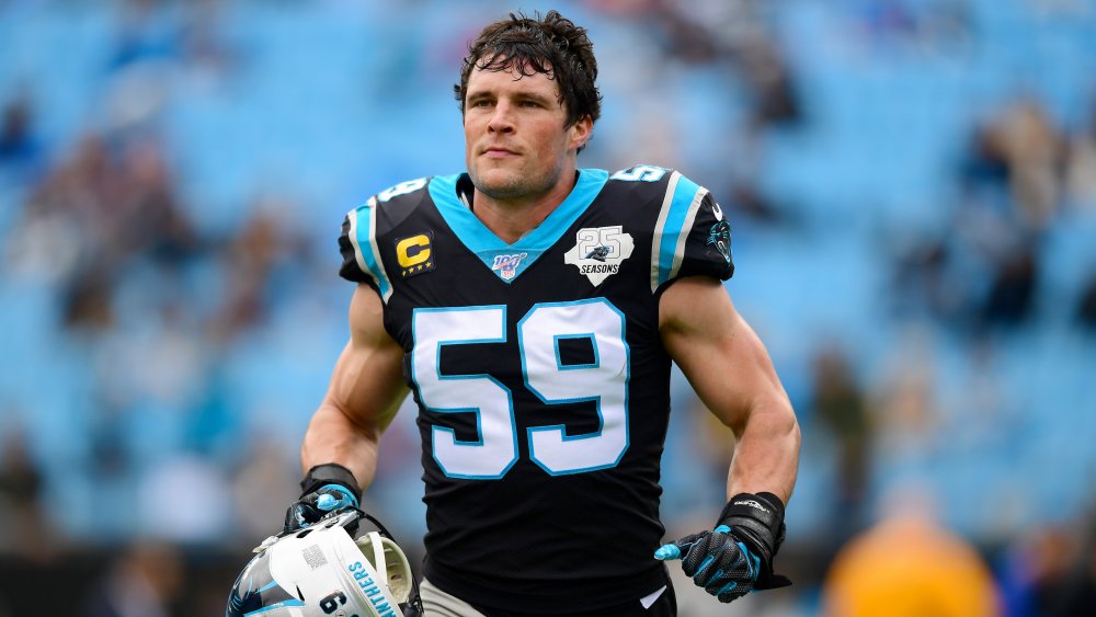 Luke Kuechly che corre sul campo, tenendo il casco