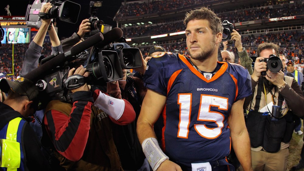 Tim Tebow in uniforme dei Denver Broncos, circondato da giornalisti