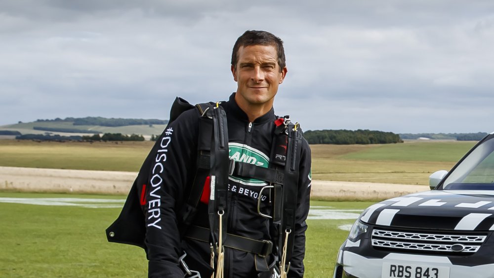 Bear Grylls in attrezzatura esterna accanto a un'auto