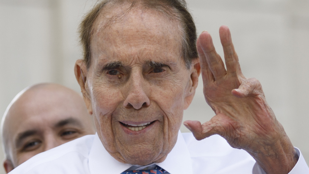 Bob Dole, sorridente, salutando, in una camicia con colletto e cravatta