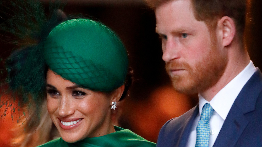 Meghan Markle in cappello verde con il principe Harry accigliato