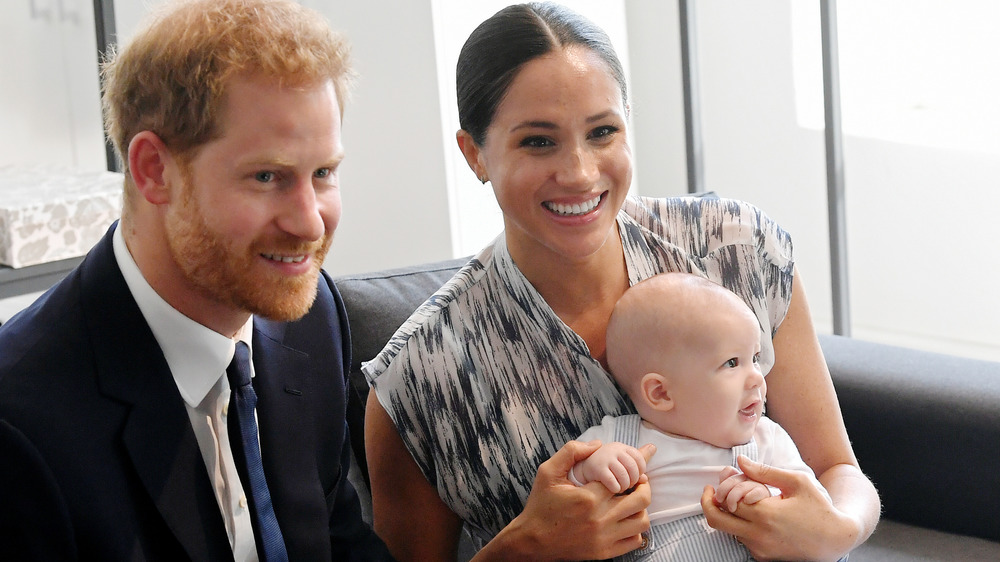 Il principe Harry seduto accanto a Meghan Markle tiene in braccio il piccolo Archie