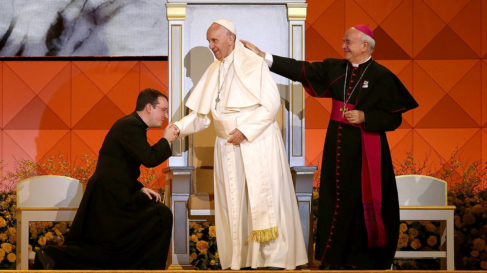 Sacerdote che bacia l'anello di Papa Francesco mentre il cardinale gli tocca la spalla