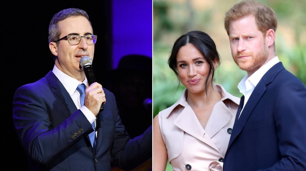 John Oliver che parla sul palco, Meghan Markle e il principe Harry guardano fuori campo