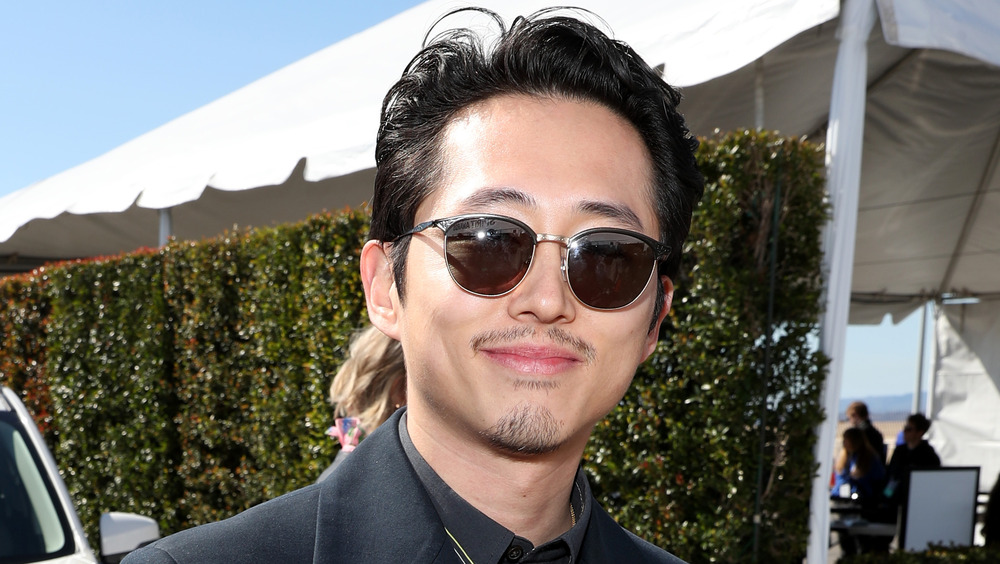 Steven Yeun sorride con gli occhiali da sole