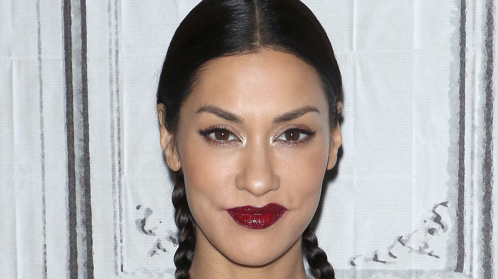 Janina Gavankar indossa rossetto rosso scuro e trecce sorridenti