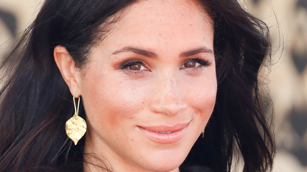 Meghan Markle sorride mentre indossa orecchini in foglia d'oro