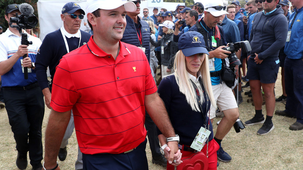 Patrick Reed e Justine Reed camminano mano nella mano, entrambi con indosso un cappello, circondati da fotografi e fan 