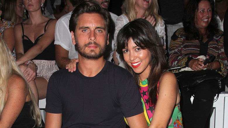 Uno Scott Disick con la faccia di pietra accanto a una sorridente Kourtney Kardashian