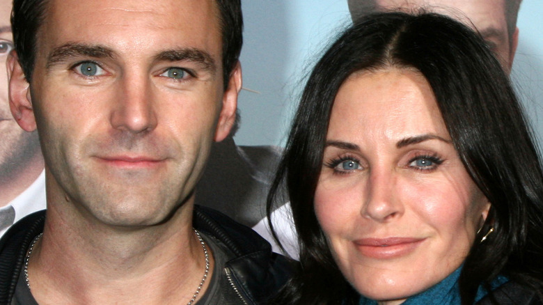 Johnny McDaid e Courteney Cox sorridono