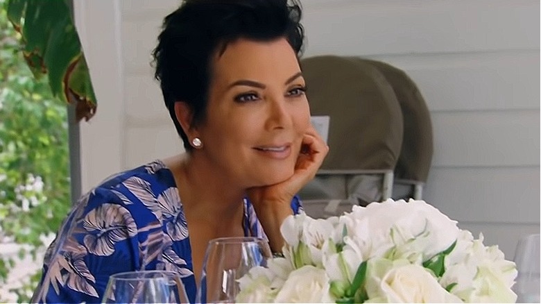Kris Jenner in maglia tropicale, accanto a fiori bianchi