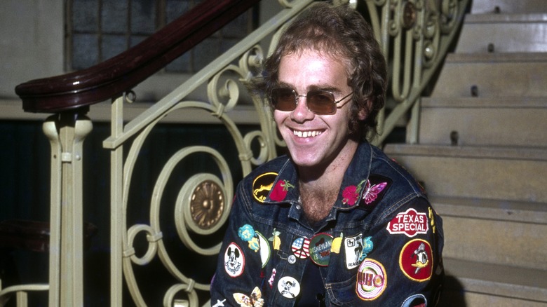 Elton John sorridente e seduto sui gradini