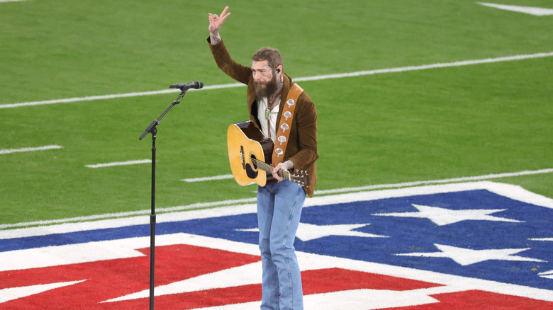 Post Malone fa il segno della pace mentre suona la chitarra sul campo di calcio