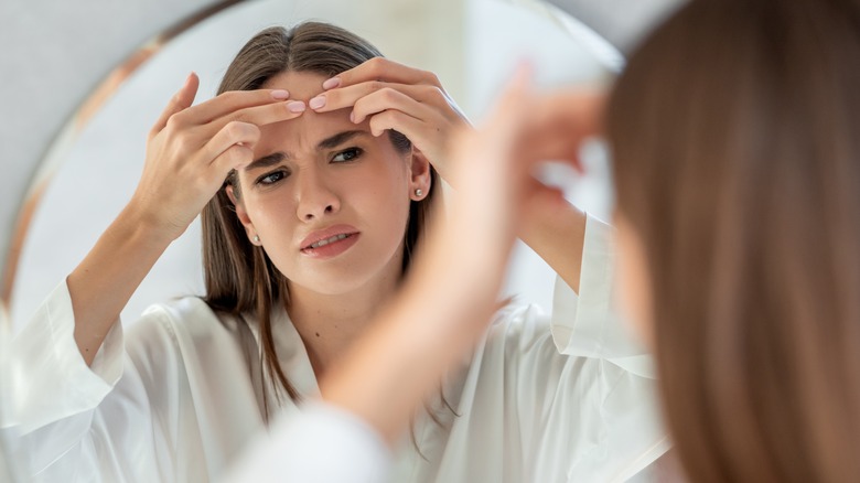 Giovane donna che guarda l'acne sulla fronte allo specchio