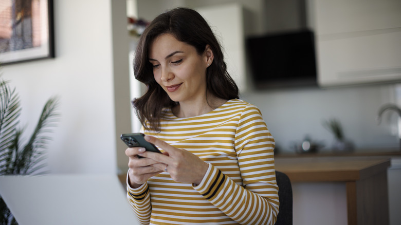 Donna che tiene il cellulare davanti allo schermo del computer portatile