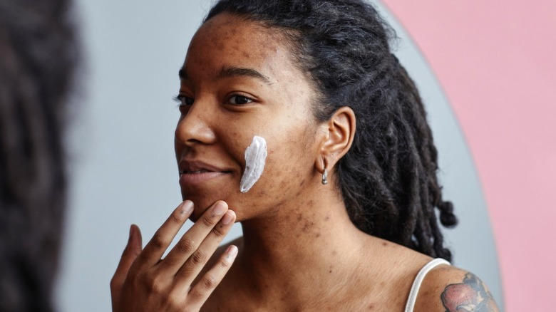 Donna con acne che applica prodotti per la cura della pelle