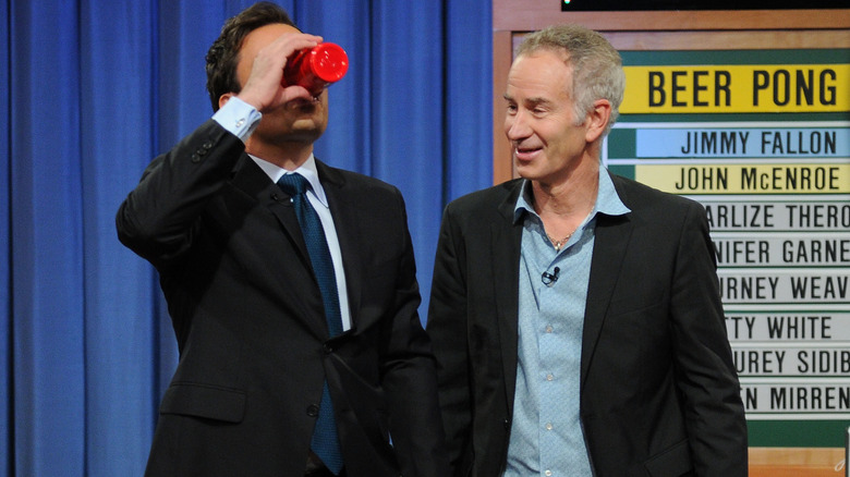 Jimmy Fallon beve da una tazza rossa mentre John McEnroe lo guarda