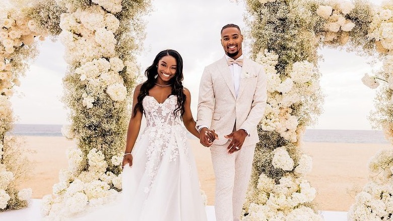 Simone Biles in un abito da sposa bianco in pizzo e Jonathan Owens in un completo beige e bianco