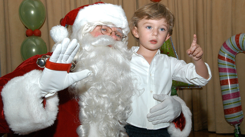 Persona in costume da Babbo Natale che saluta, Barron Trump che indica