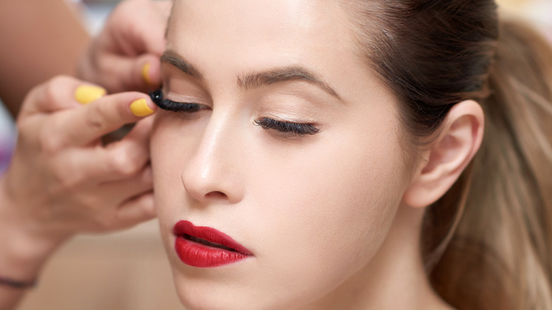 Donna con rossetto rosso che si fa applicare le ciglia finte