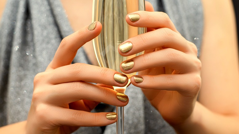 Mani con manicure dorata che tengono champagne