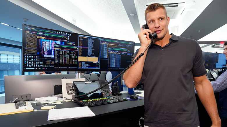 Rob Gronkowski indossa una polo grigia mentre parla al telefono