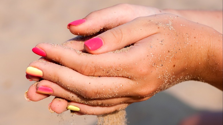 Mani abbronzate e curate che tengono la sabbia