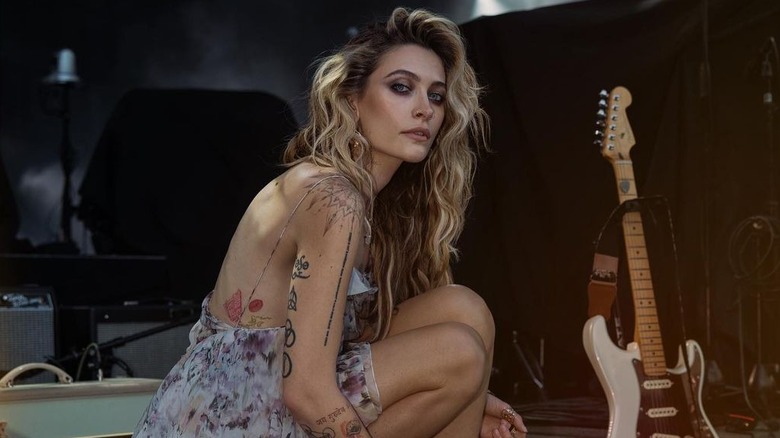 Paris Jackson indossa un abito floreale con spalline e posa accanto a una chitarra