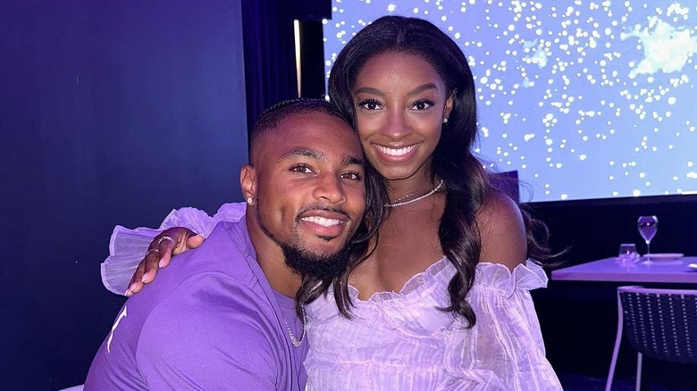 Jonathan Owens indossa una camicia viola e Simone Biles indossa una svolazzante blusa viola