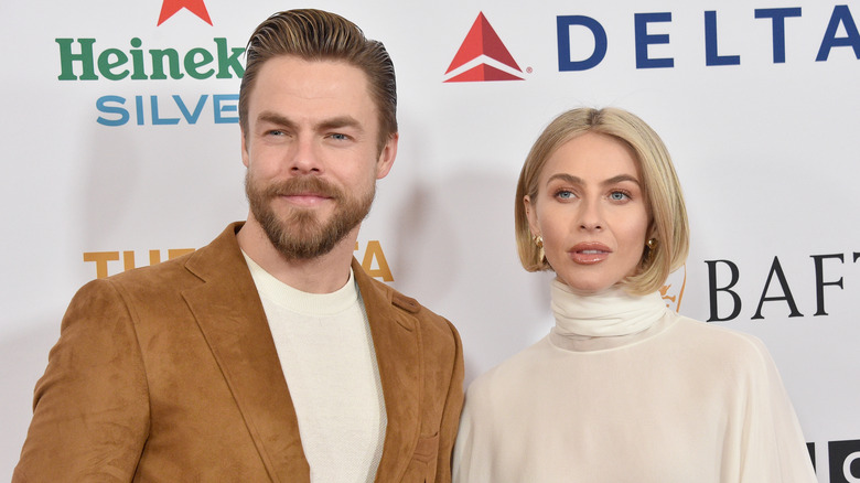 Derek Hough indossa una giacca scamosciata marrone e una camicia bianca con Julianne Hough che indossa un dolcevita color crema