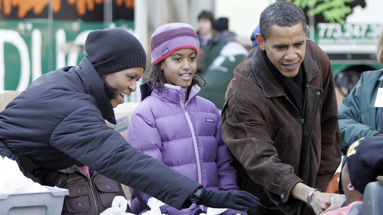 Michelle Obama indossa un cappotto invernale blu e un berretto nero con Malia Obama che indossa un cappotto invernale viola e un cappello abbinato con Barack Obama che indossa un cappotto marrone