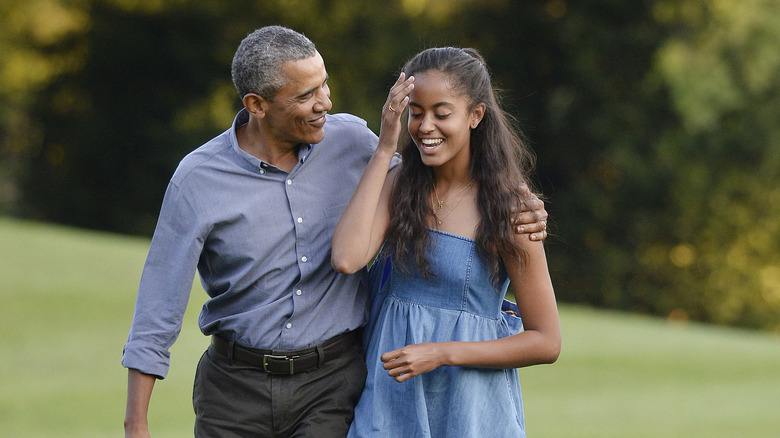 Barack Obama indossa una camicia grigia abbottonata e pantaloni marroni con Malia Obama che indossa un prendisole in denim con spalline