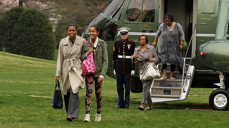 Michelle Obama indossa un cappotto marrone chiaro e pantaloni grigi con Malia Obama che indossa una giacca verde e leggings floreali