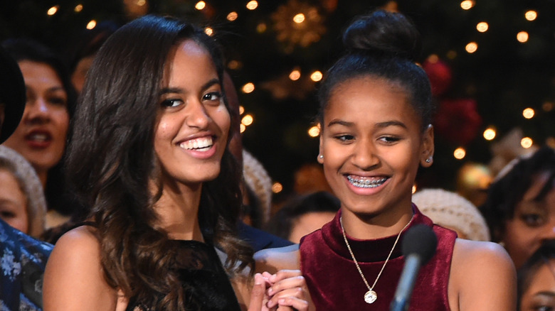 Malia Obama indossa un abito nero senza spalline con Sasha Obama che indossa un abito rosso di velluto a collo alto