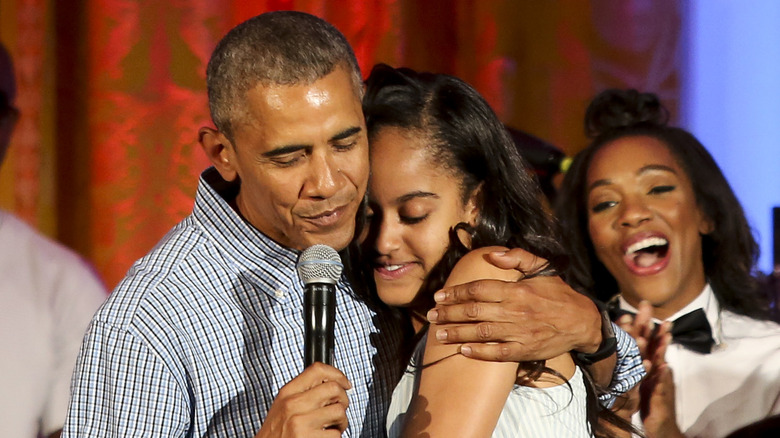 Barack Obama indossa una camicia a righe con bottoni e abbraccia la figlia Malia, che indossa un abito a righe senza spalline