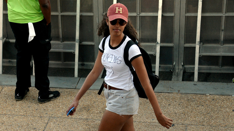 Malia Obama indossa una maglietta bianca, pantaloncini di jeans e un berretto da baseball cremisi