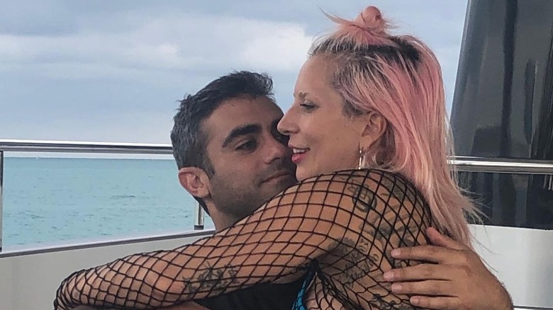 Lady Gaga indossa un top a rete seduta con Michael Polansky che indossa una maglietta scura vicino all'acqua