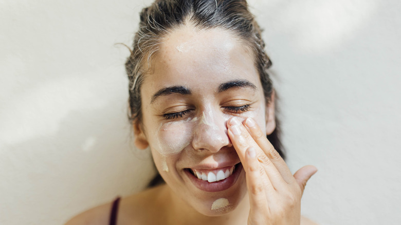 Donna sorridente che applica la crema solare sul viso