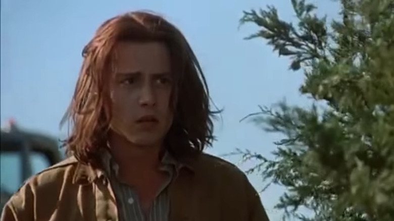 Johnny Depp con i capelli lunghi indossa una giacca marrone e una camicia button-down a righe